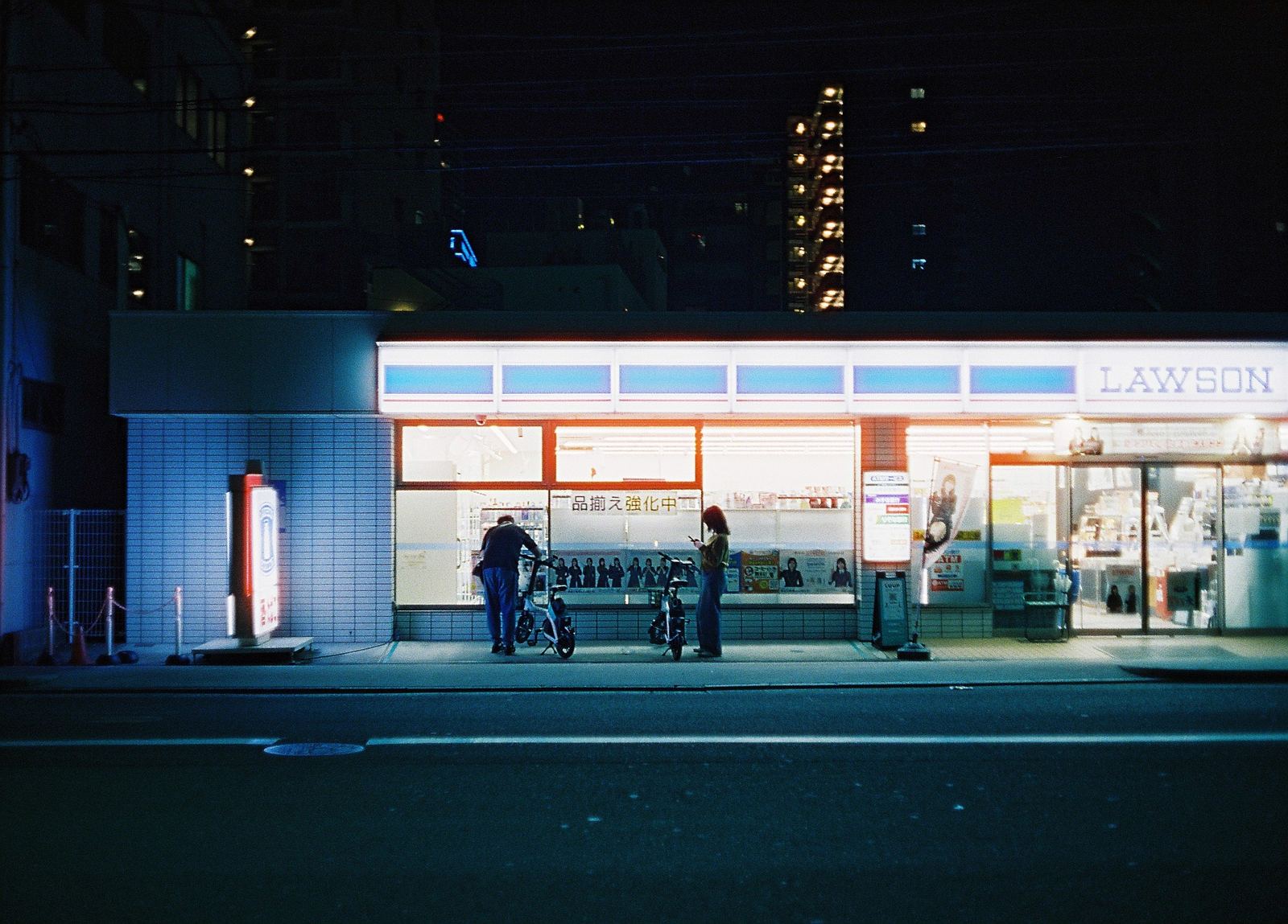 A brightly lit convenience store glowing across an Osaka street at night